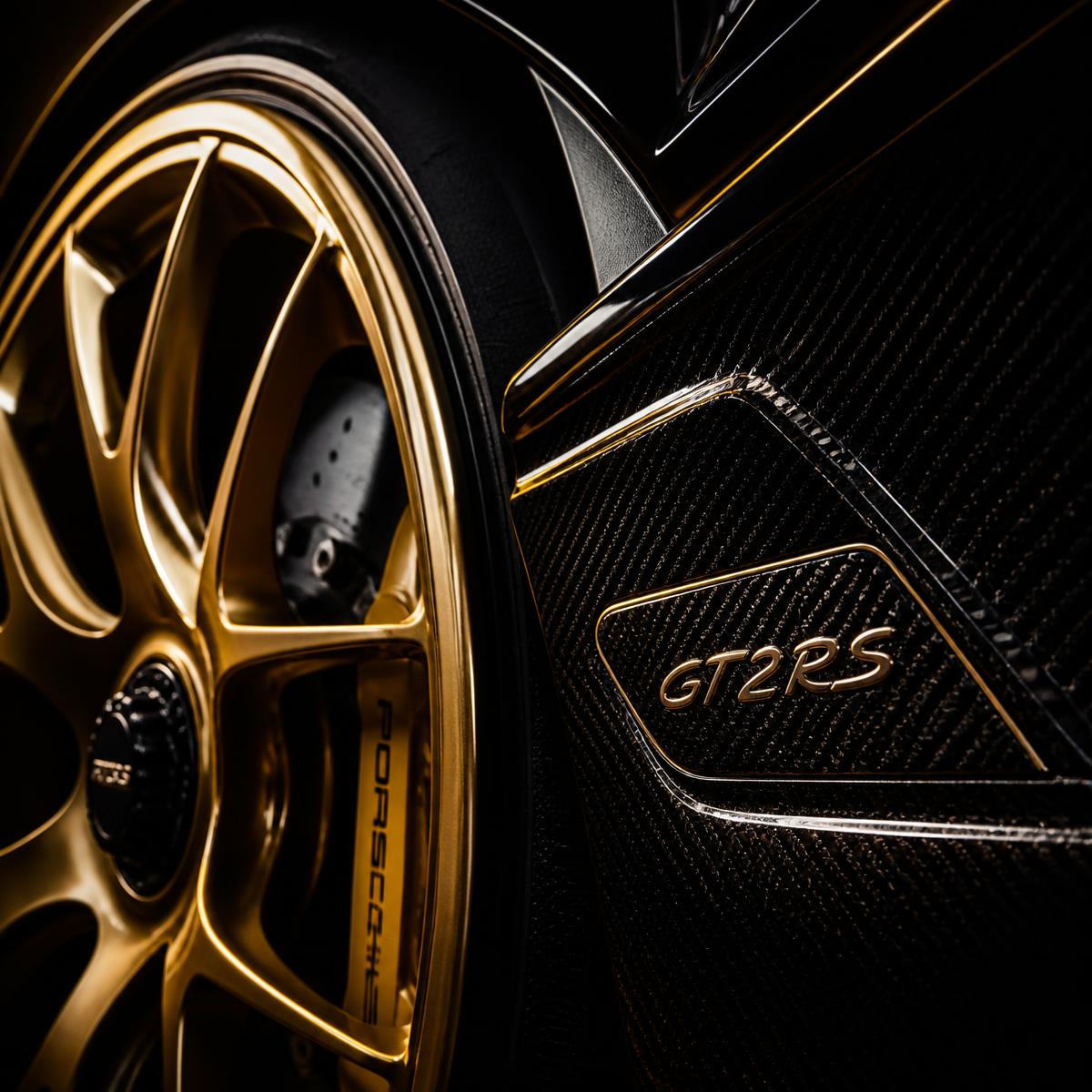 Close-up of a gold sports car wheel and carbon badge under studio light